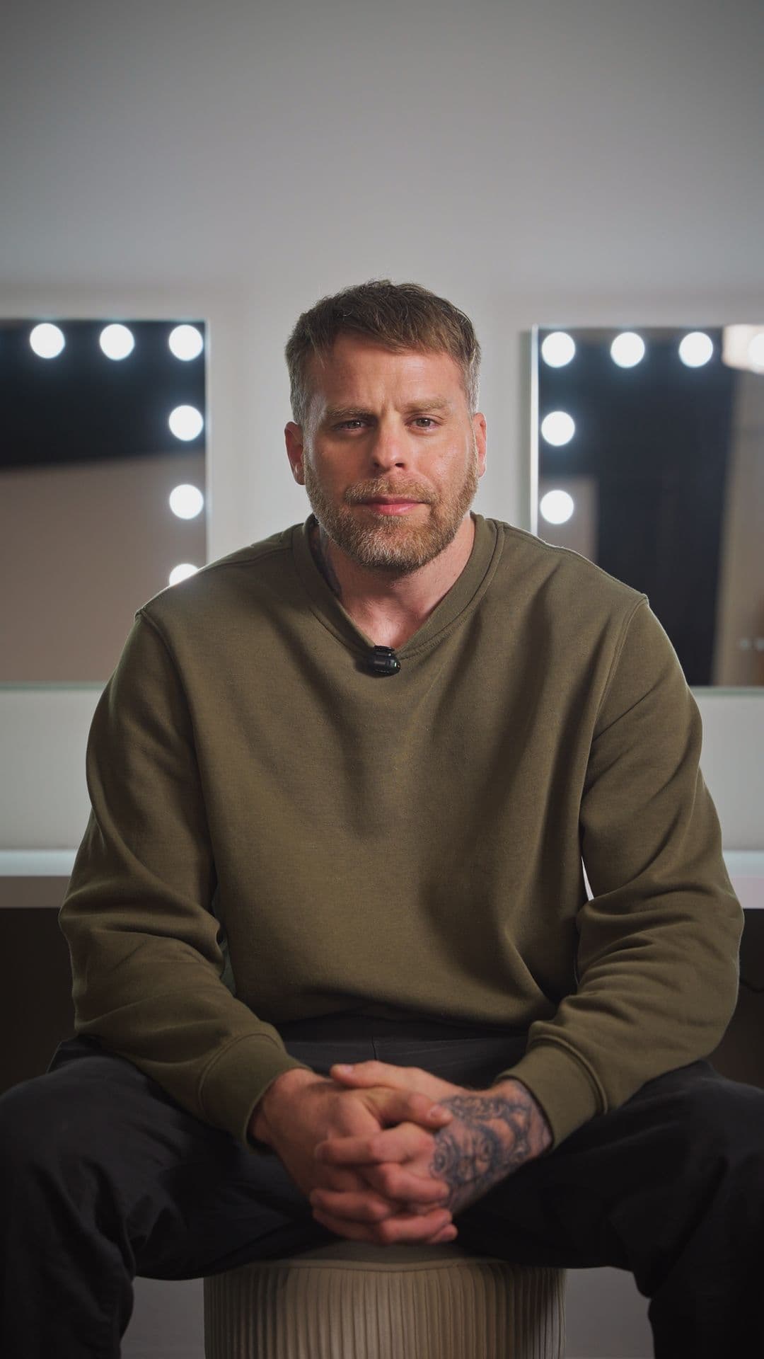 Paul Alexander standing in the studio in a black t-shirt, arms folded, directional rim light behind him.